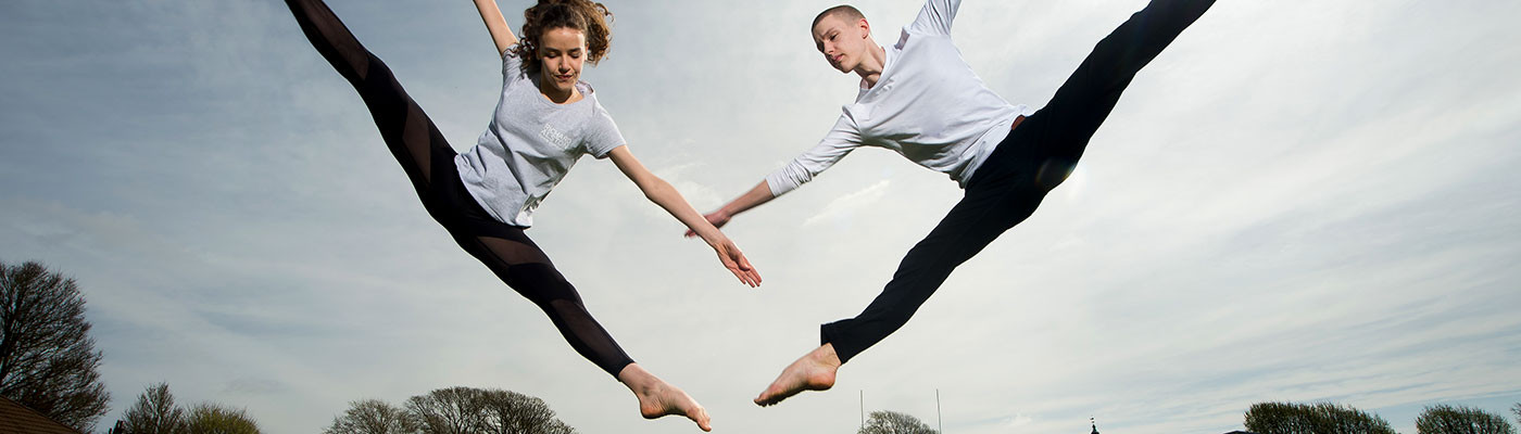 Two dance students performing a dance move in mid-air 
