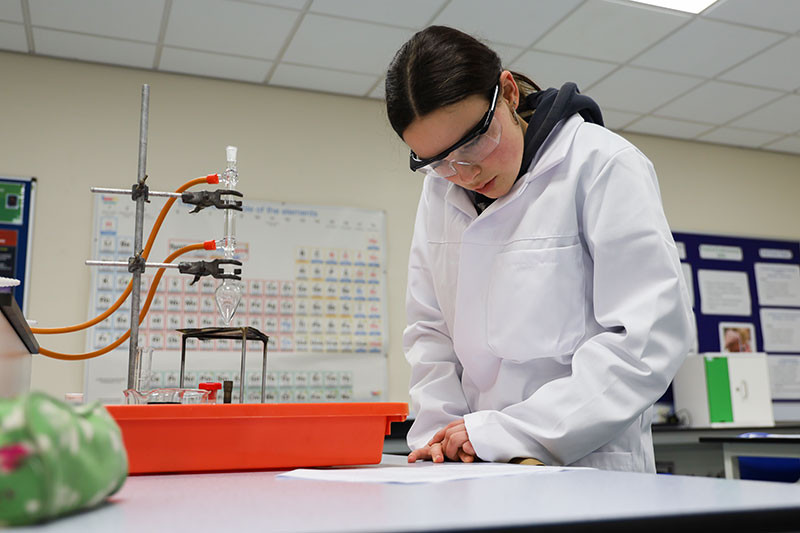 Having set up her refluxing apparatus, Lola double-checks the quantities of reagents she needs before collecting them. 